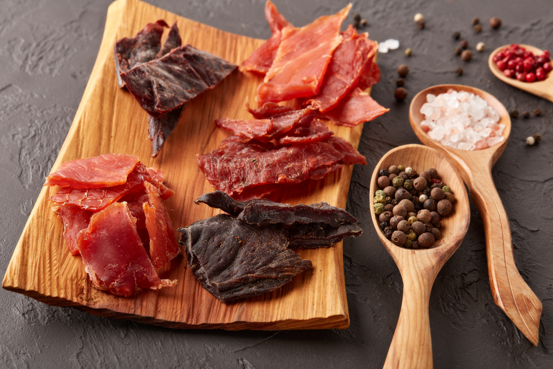 Alt Text: Mixed beef jerky slices with black pepper, sea salt, and spices on a dark background
