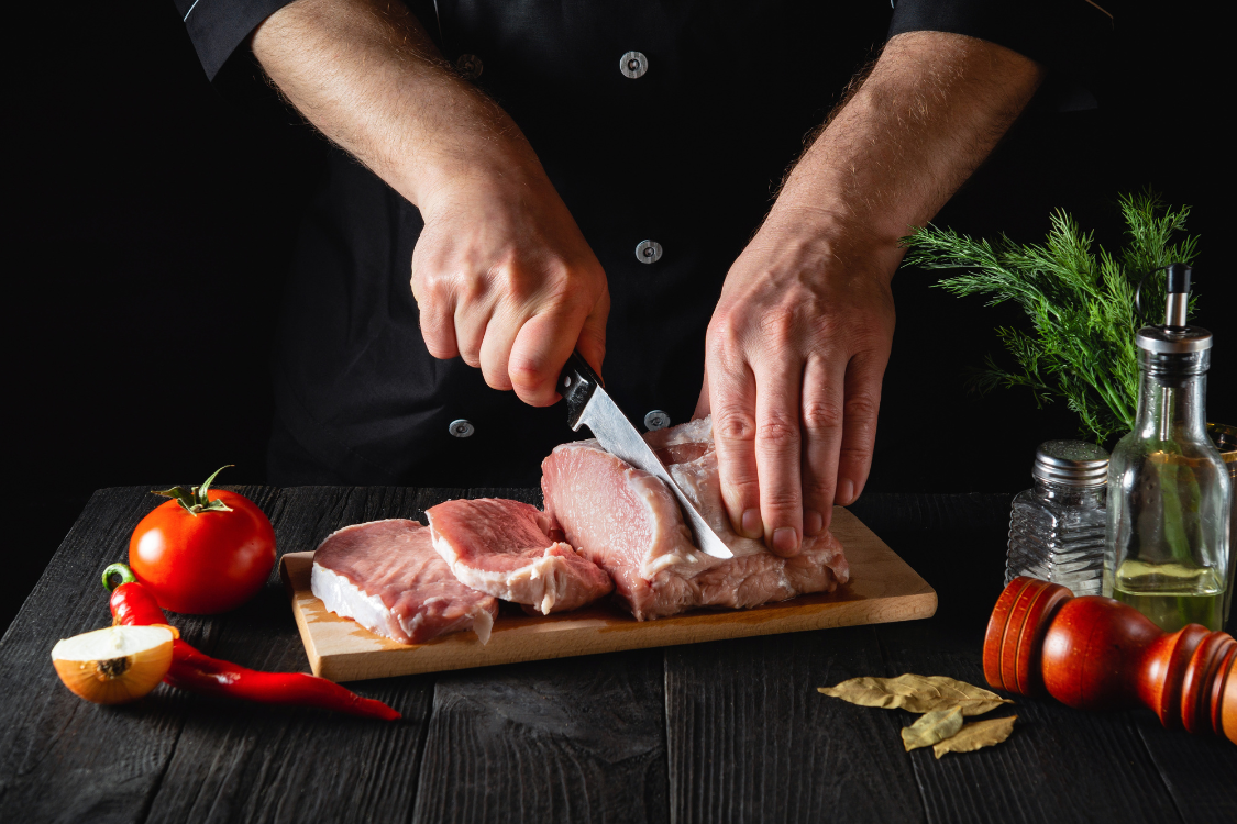 Chef slicing raw beef on a cutting board to prepare meat for jerky