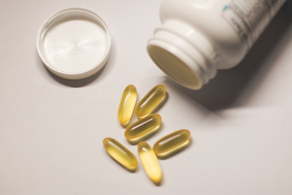 Olive oil softgel capsules spilled from a bottle, representing olive oil as a dietary supplement.