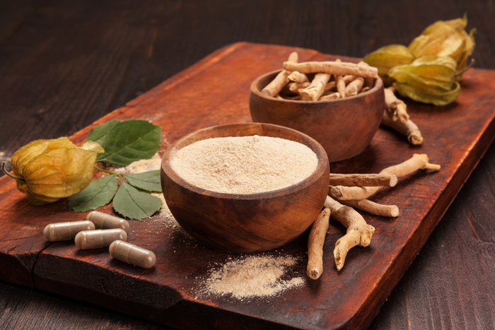 A wooden tray of Ashwagandha powder, capsules, and roots.
