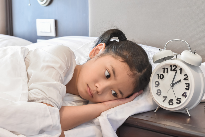 Young girl with autism having trouble falling asleep and staring at clock