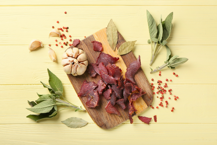 Beef jerky on a wooden board surrounded by spices.