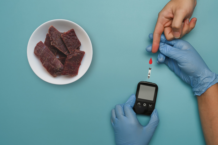 A glucose meter showing 148 mg/dL next to a hand and lancet device, related to blood sugar tracking after eating beef jerky