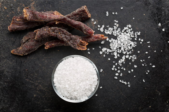 Strips of beef jerky beside a bowl of coarse salt – highlighting high sodium content in processed meats.