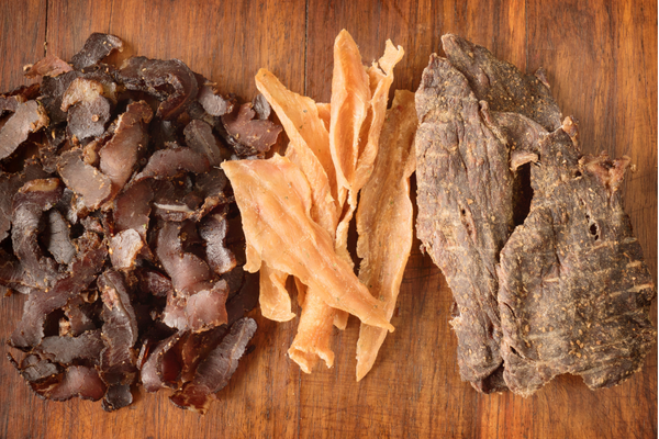 An assortment of beef jerky pieces on a wooden board, highlighting different flavors and textures.