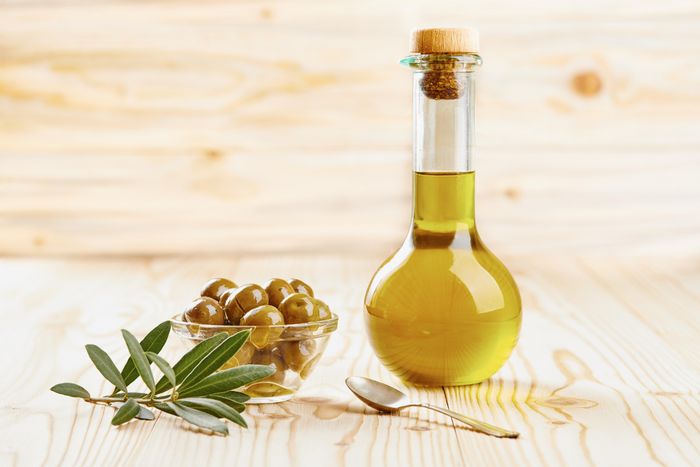 A bottle of olive oil next to a bowl of green olives and olive leaves on a wooden table, representing natural olive oil ingredients.