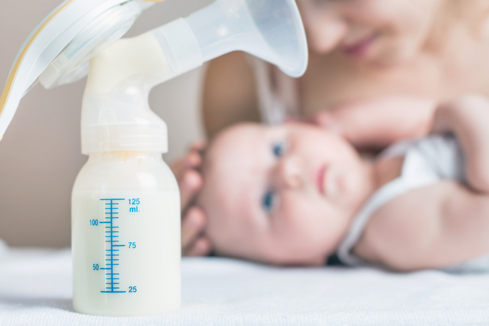 Breastfeeding mother with baby and breast pump collecting expressed milk