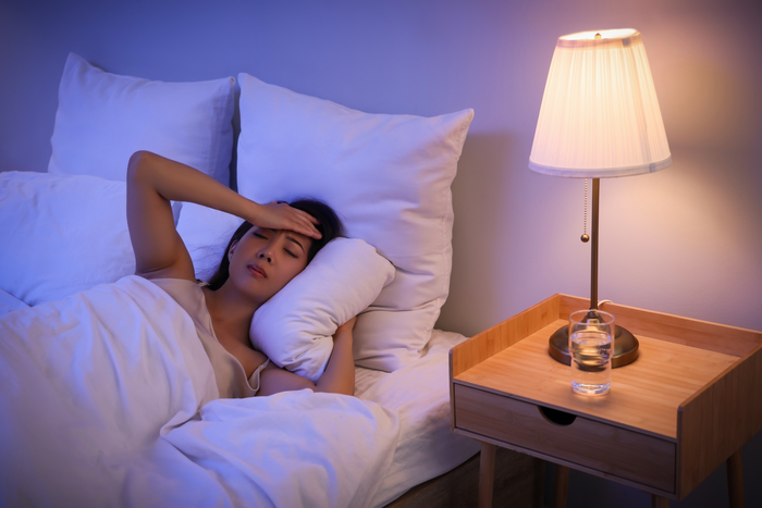 Restless person lying awake in bed with hand on forehead, illustrating insomnia.