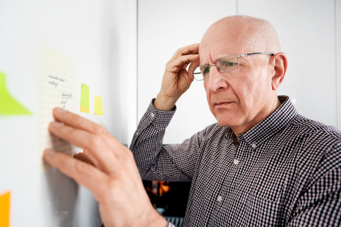 Older man looking confused at post-it notes, visually representing memory concerns or cognitive function issues.
