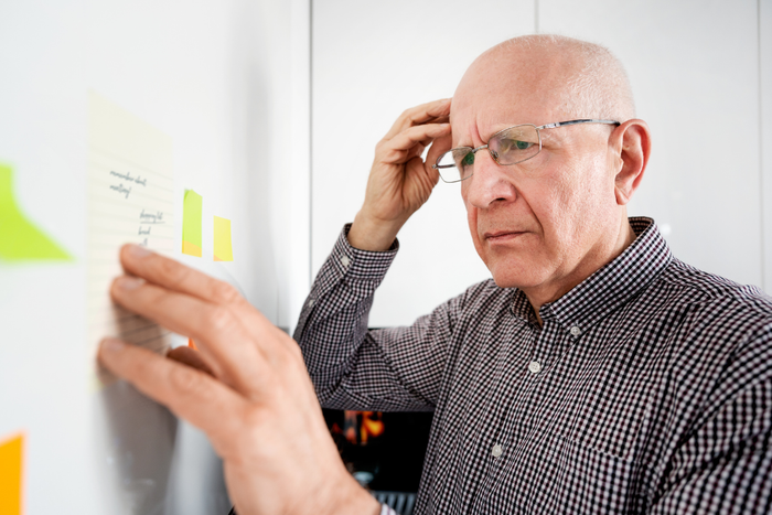 Older man looking confused at post-it notes, visually representing memory concerns or cognitive function issues.