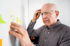 Older man looking confused at post-it notes, visually representing memory concerns or cognitive function issues.
