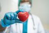 Gloved healthcare professional holding a red heart model in focus, representing heart health concerns related to melatonin and questions about heart failure.