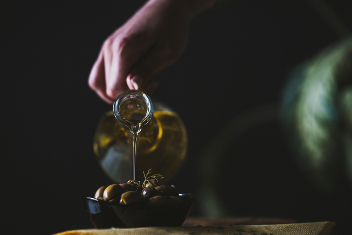A person pouring olive oil on a bunch of olives.
