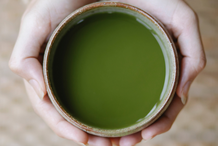 Hands holding a bowl of freshly prepared matcha tea, showing its vibrant green color