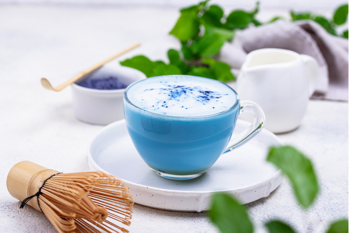 Frothy blue matcha latte made with butterfly pea powder on a white tray