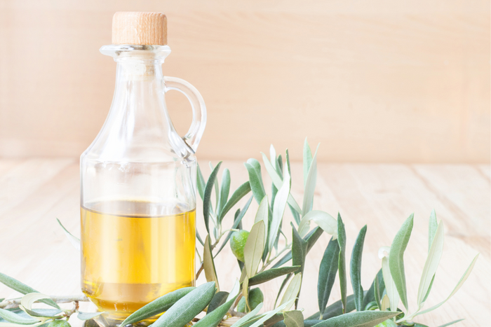 Glass bottle of olive oil with fresh olive branches on a wooden table