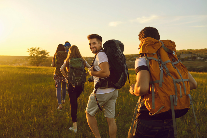 Group of hikers with backpacks walking through a grassy trail at sunset