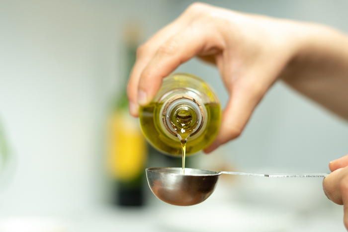 Woman pouring cooking oil on a measuring spoon.