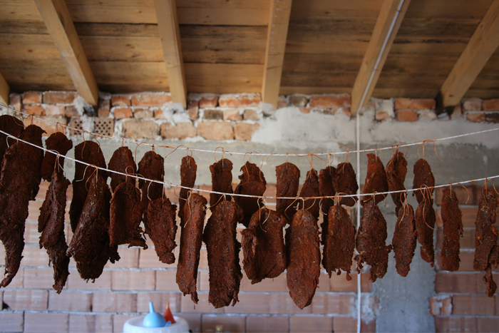 Homemade beef jerky strips hanging on a string to dry in a rustic setting