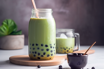 Matcha green tea bubble tea in a glass jar with tapioca pearls, ice, and a straw, served with extra boba on the side.