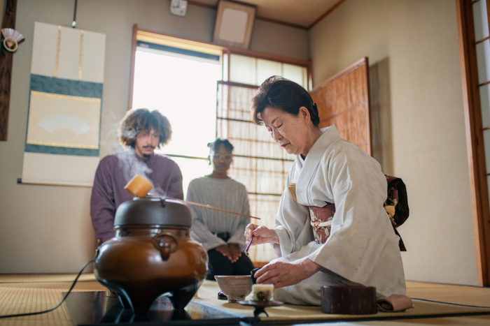 Tea master in kimono preparing matcha during cultural tea ceremony with guests