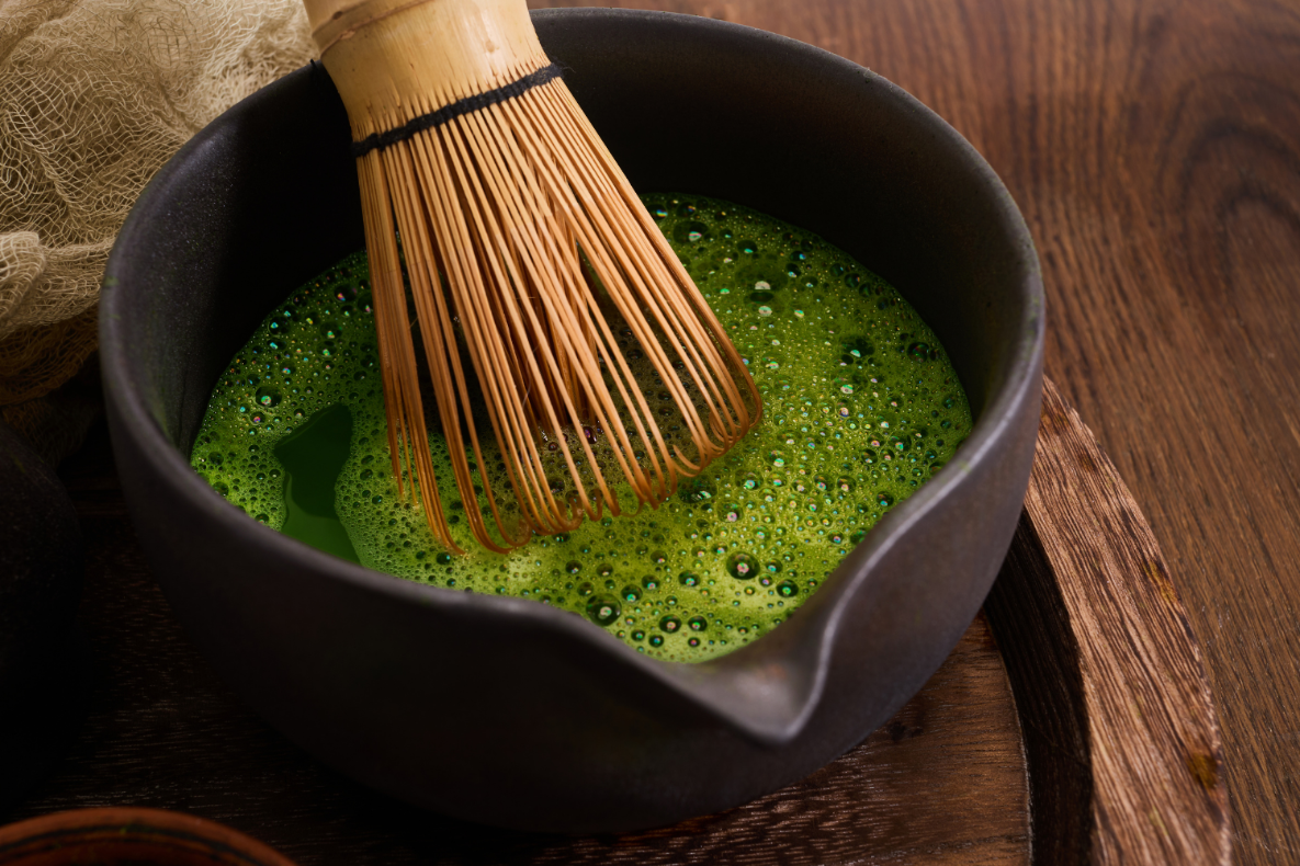 A bamboo whisk rests in a black bowl of frothy green matcha tea.