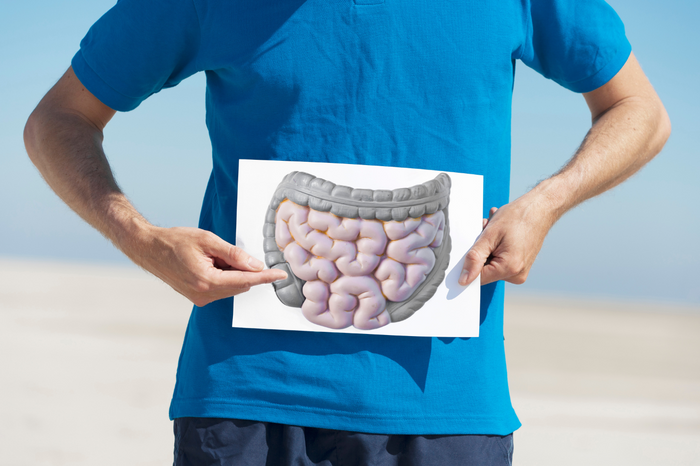 Man in a blue shirt holding a digestive system illustration over his abdomen, symbolizing gut health and leaky gut awareness.
