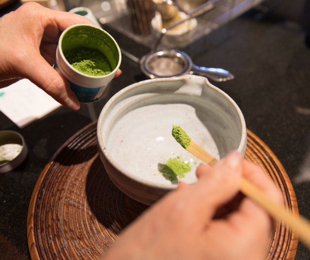 Hands preparing matcha tea using a bamboo scoop and bowl to measure matcha calories per serving