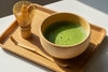 Wooden matcha bowl filled with frothy green matcha tea on a wooden tray.