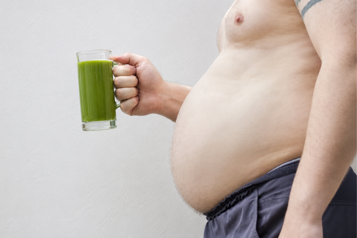 A person holding a glass of matcha green tea with a prominent belly.
