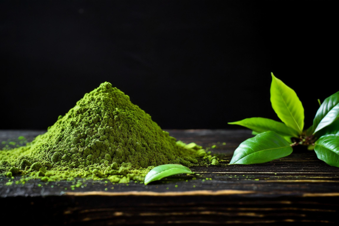 Vibrant pile of matcha powder next to fresh green tea leaves, showing the final product of matcha before it is prepared and consumed.