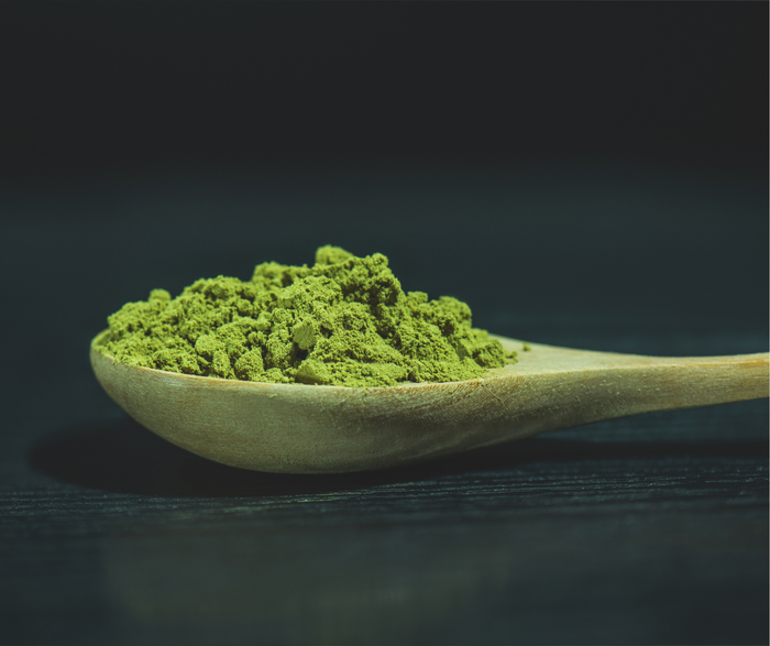 Wooden spoon filled with vibrant green matcha powder, showing low calories per teaspoon.