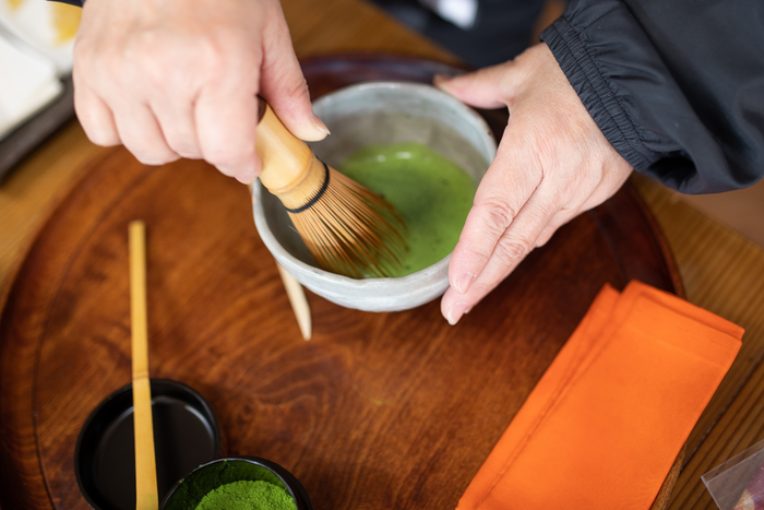 Hands using a bamboo whisk to prepare matcha green tea in a traditional bowl