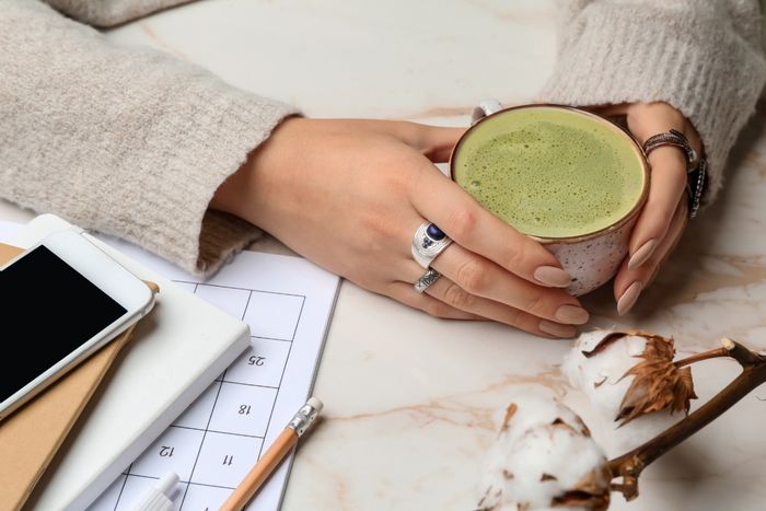 Person holding a cup of matcha with notebooks on a desk.