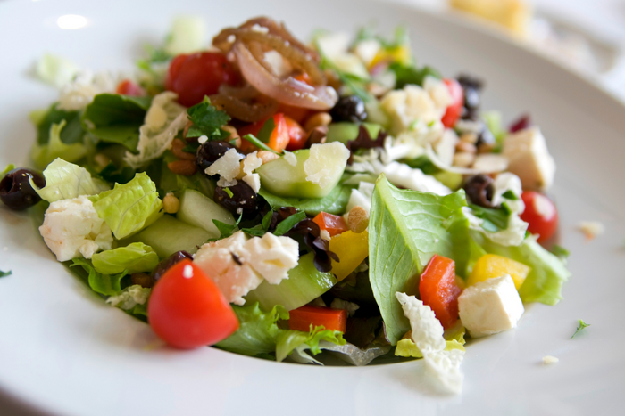 Mediterranean salad with feta cheese, kalamata olives, cherry tomatoes, and fresh greens on a white plate
