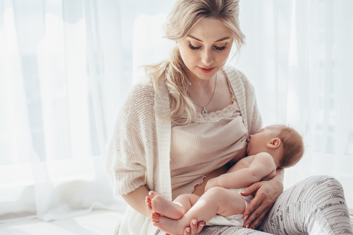 A breastfeeding mother in a softly lit room gently cradles her baby at night, symbolizing natural sleep support and the role of melatonin in breast milk.
