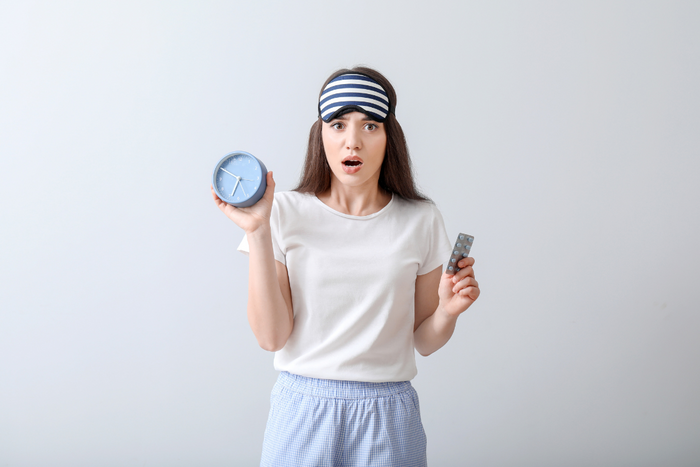 Woman in sleepwear looking confused, holding a clock and melatonin tablets