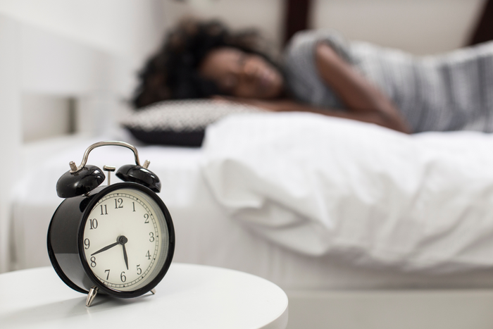 Woman sleeping with alarm clock on the foreground.