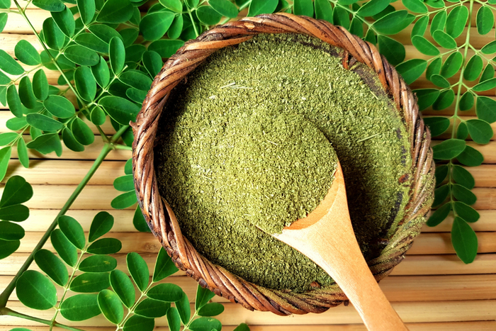 Bowl of moringa powder, surrounded by moringa leaves.