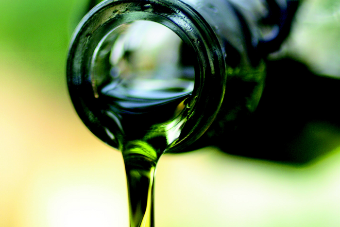 Olive oil pouring from a green bottle.