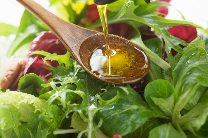 Olive oil being poured onto a fresh salad.
