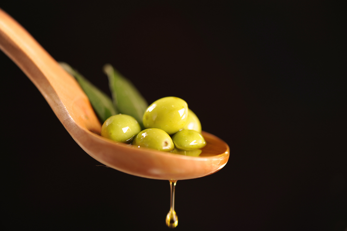 Fresh green olives with olive oil dripping from a wooden spoon