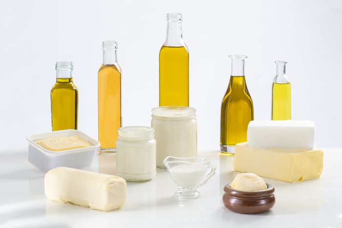 Various types of butter and olive oil in jars and bottles on a white background for cooking and health comparison