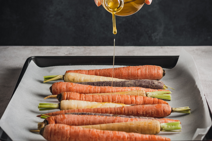 Person pouring oil on vegetables.