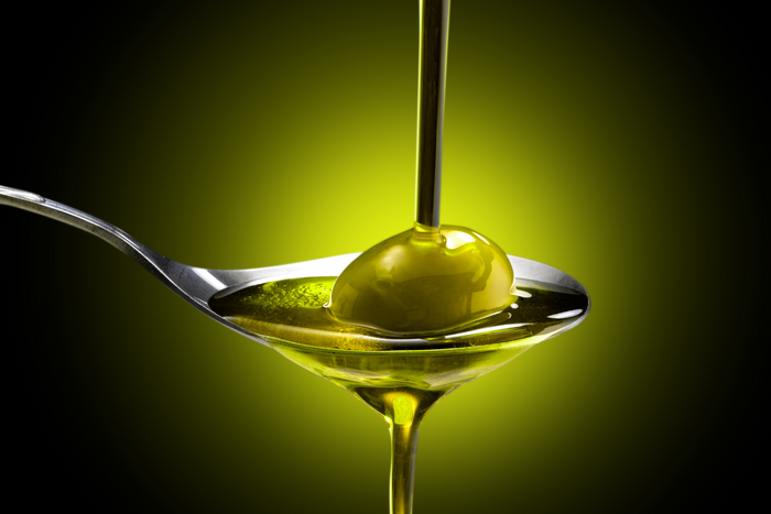 Olive oil being poured on a spoon with a piece of olive.