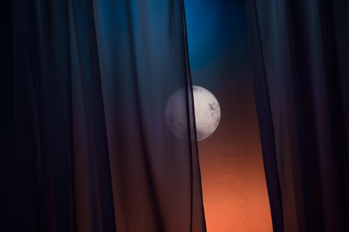 Night sky with bright moon through a window curtain.