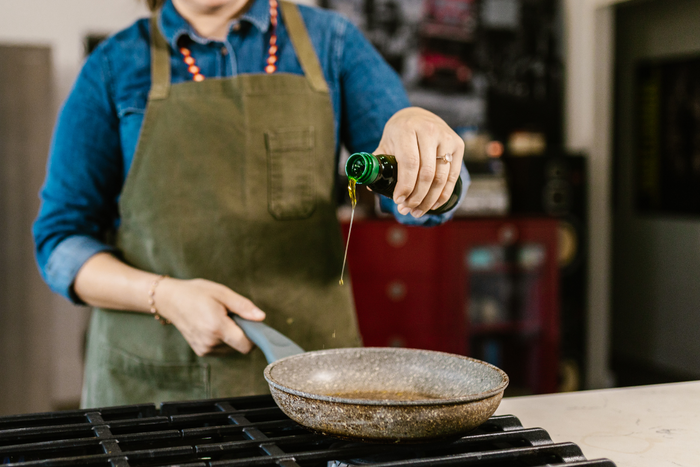 Person pouring extra virgin olive oil into a pan for sautéing on stovetop