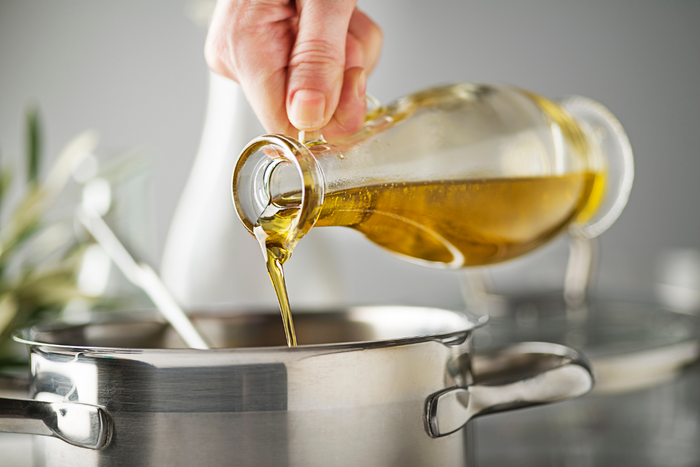 Hand pouring extra virgin olive oil into a stainless steel pot