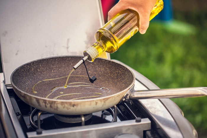 Hand pouring olive oil into a heated pan on an outdoor stove