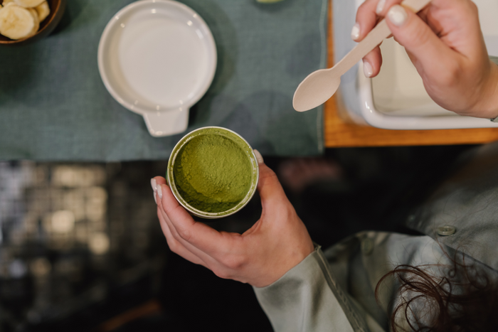 Person scooping vibrant green matcha powder from a container